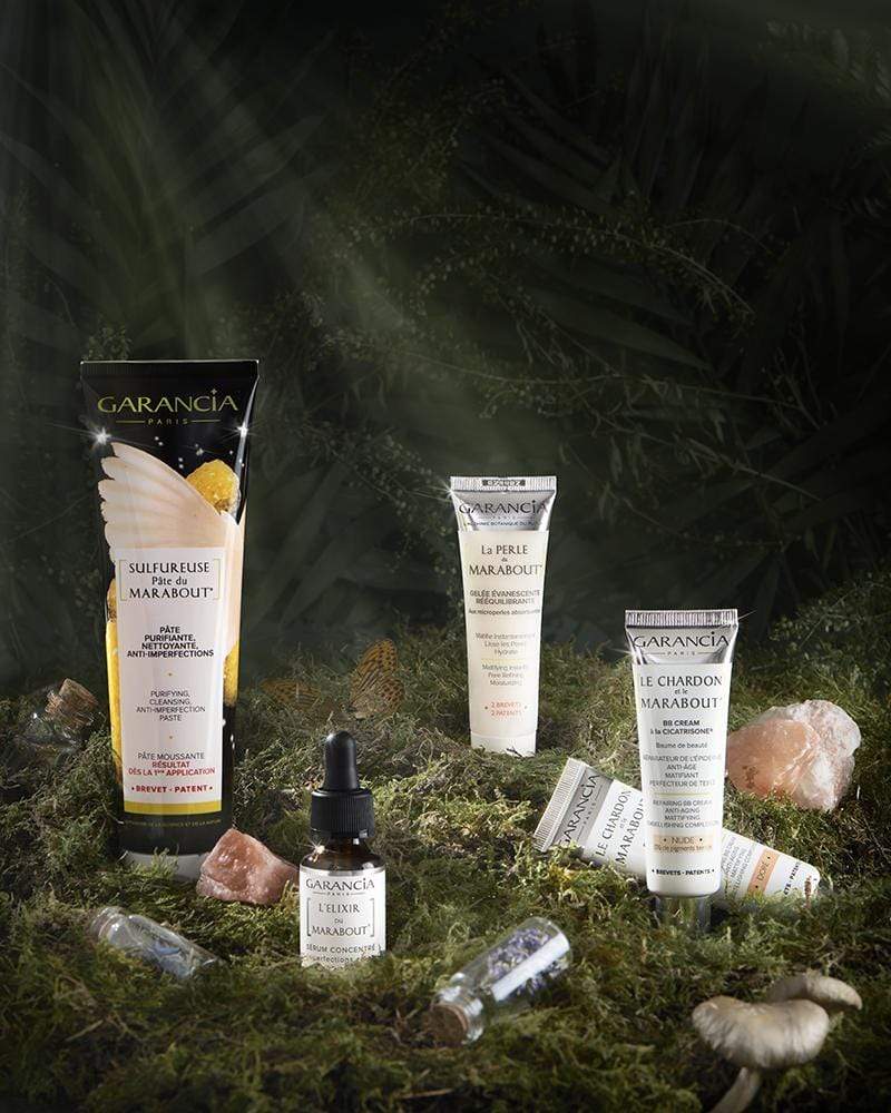 Ensemble de soins anti-imperfections Garancia comprenant la Sulfureuse Pâte du Marabout, l'Élixir du Marabout, La Perle du Marabout et Le Chardon et le Marabout, mis en scène dans un sous-bois magique avec mousse et cristaux.
