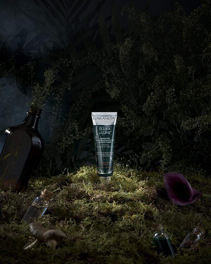 Laboratoire Garancia Crème de jour ÉCLAIR DE LUNE : soin concentré anti-taches et anti-âge mains et visage, mis en scène sur un tapis de mousse dans une forêt mystérieuse et sombre.